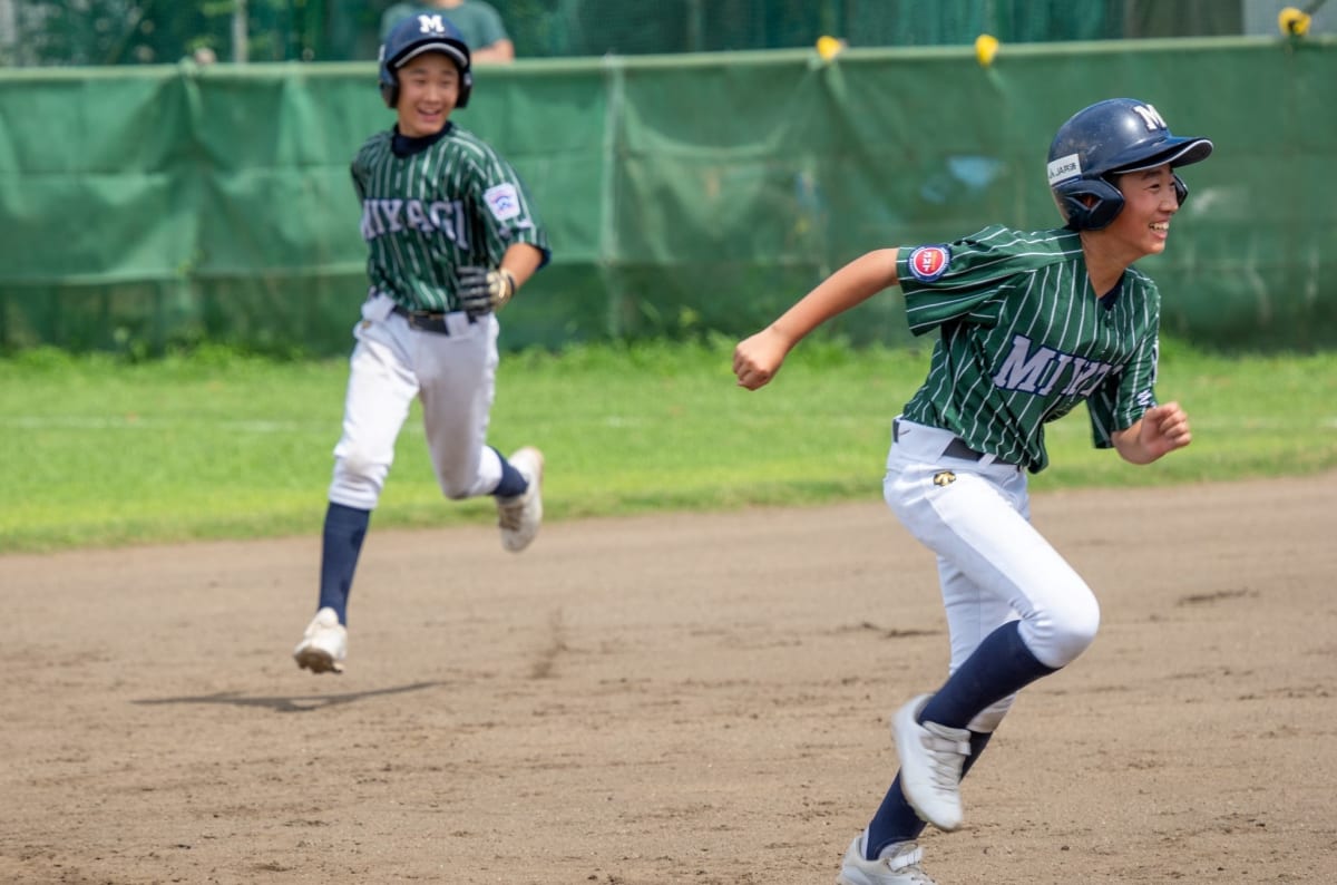 リトルリーグの野球チームがグラウンドで撮る集合写真。青いユニフォームの子供たちが笑顔で並び、子供の成長に繋がるチームワークを表現。