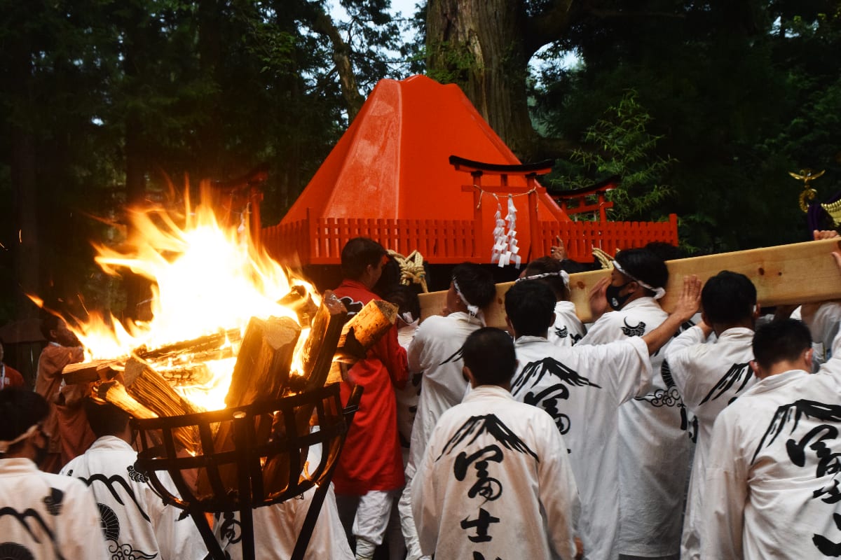 吉田の火祭りで燃え盛る巨大な松明。夜空を焦がす炎の後ろに、雄大な富士山のシルエットが浮かび上がる。